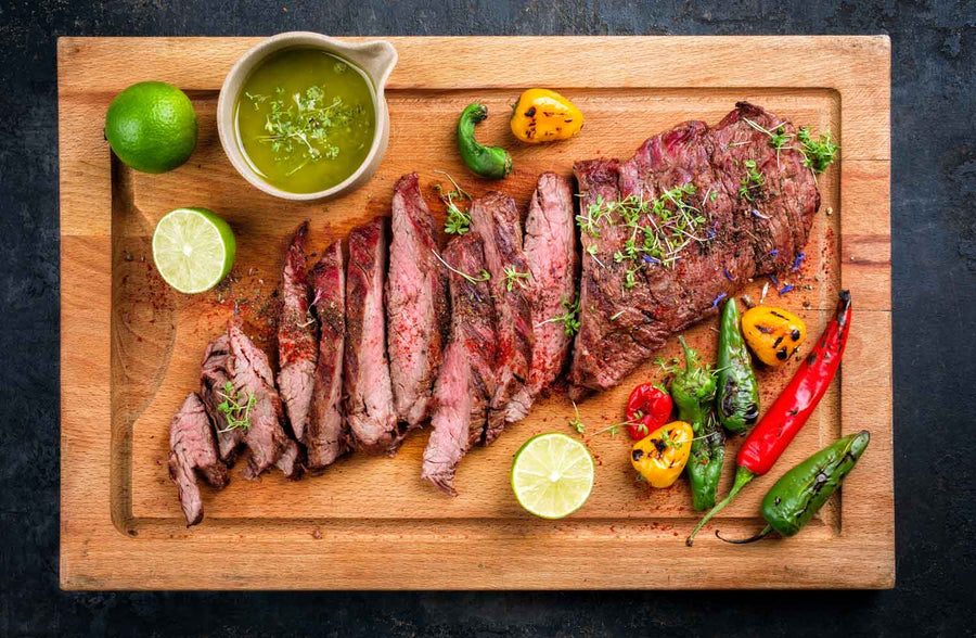 Bavette Steak grilled and placed on a cutting board with grilled peppers